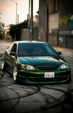 a green car parked on the street in front of a building with graffiti written on it