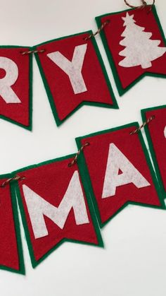 three red and green christmas banners with white letters on them hanging from twine strings