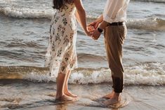 a man and woman holding hands while standing in the water at the edge of the beach