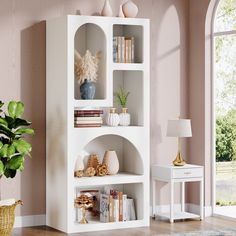 a white shelf with books and vases on it in front of a pink wall