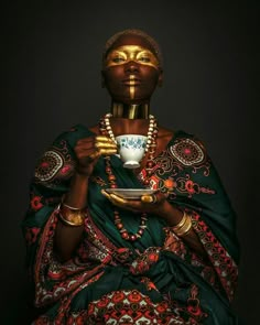 an african woman holding a cup and saucer in her hands with gold paint on her face