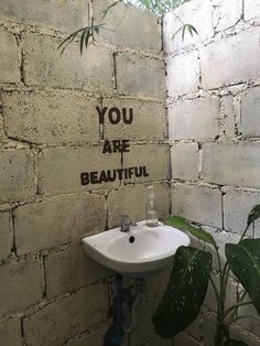 a white sink sitting next to a wall with graffiti on it's side and the words you are beautiful above it