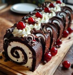 a chocolate roll with cherries and whipped cream on a wooden cutting board next to plates