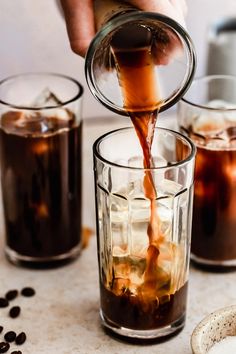 someone pours coffee into two glasses filled with ice and coffee beans on the table