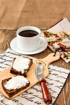 two pieces of bread on a wooden cutting board next to a cup of coffee and book