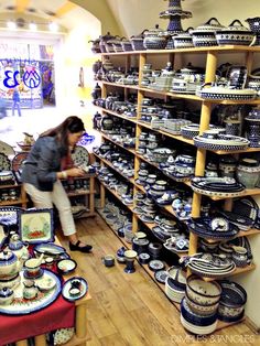 a woman looking at plates on display in a store with shelves full of dishes and vases