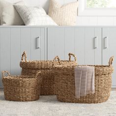 three woven baskets with handles on the floor in front of a white bed and dresser