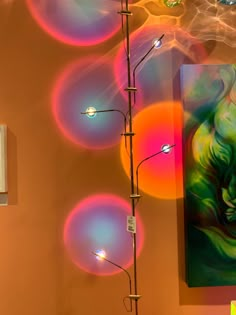 an art piece is displayed in front of a wall with colorful circles on it and a painting hanging from the ceiling