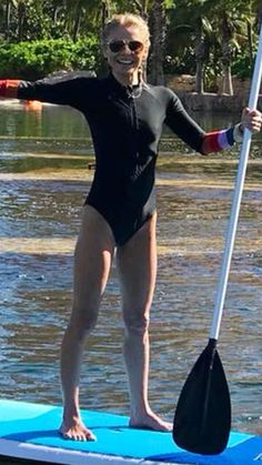 a woman in a wet suit standing on a paddle board with her arms out and holding a oar