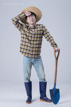 a man in plaid shirt holding a shovel and wearing blue boots with hat on his head