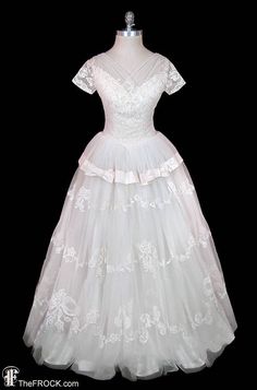 a white wedding dress on a mannequin head stand in front of a black background