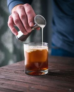 a person pouring something into a glass on top of a wooden table with a spoon