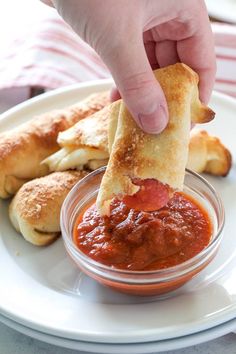 a person dipping some food into a small bowl on a plate with breadsticks