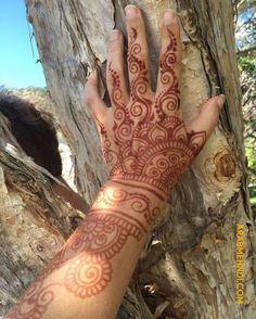 a person's hand with henna on it next to a tree and some branches