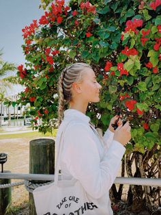 a woman holding onto a white bag while standing next to a tree with red flowers