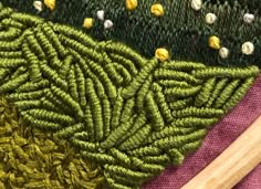 close up view of green and yellow fabric with wooden needles on it, next to another piece of art work