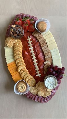 a football shaped platter with cheese, crackers, meats and fruit on it