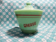 a green crock with the word grease on it sitting on a blue and white checkered tablecloth