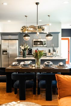 a dining room table with place settings in front of an oven and refrigerator, surrounded by blue chairs