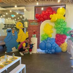 children are sitting in front of balloons and sesame street characters on the wall behind them