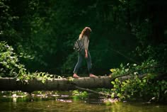 a woman walking across a fallen log over a river