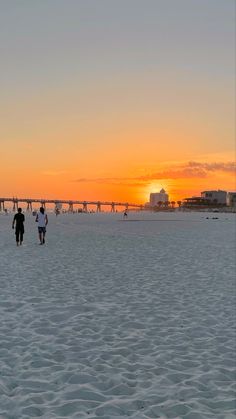 two people walking on the beach at sunset