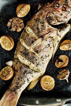 a fish sitting on top of a grill next to sliced lemons and other food