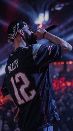 a man with a baseball cap on holding a microphone in front of an audience at a sporting event