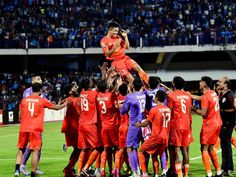 a group of men standing on top of each other in front of a soccer field