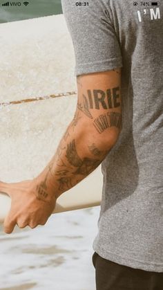 a man with tattoos on his arm holding a surfboard