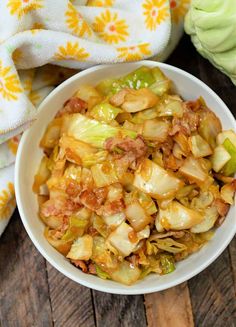 a bowl filled with cabbage and meat on top of a wooden table next to a towel