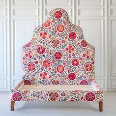 an upholstered bench with colorful designs on the back and sides, sitting in front of a white wall