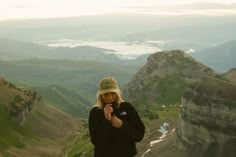 a person standing on top of a mountain with a cell phone in their hand and looking at the camera