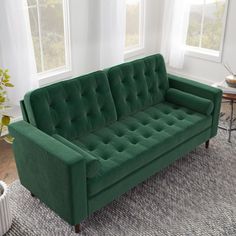 a green couch sitting on top of a rug in a living room next to two windows