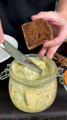 a person holding a knife and spreading spread on bread in a jar with another hand