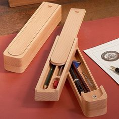 two wooden boxes with pens and pencils in them sitting on a red tablecloth