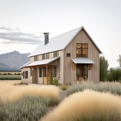 a house in the middle of a field with tall grass and mountains in the background