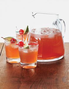 three glasses filled with liquid and garnished with cherries sit on a wooden table