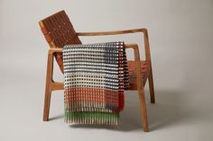 a wooden chair with a multicolored blanket on it's back and arm