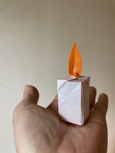 a hand holding an origami object in it's left hand, with one orange piece on top