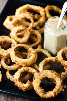 some onion rings are on a black plate with a jar of ranch dressing next to it