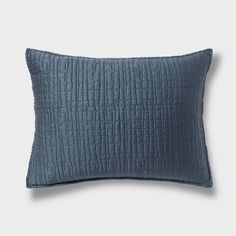 the blue quilted pillow is shown in front of a white wall and grey background