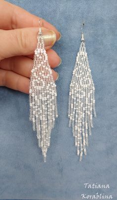 a pair of white beaded tasseled earrings on top of a blue cloth