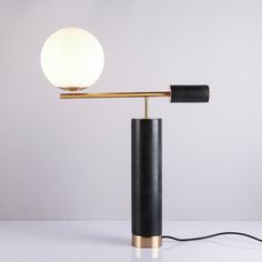 a black and gold lamp with a white ball on the top is sitting on a table