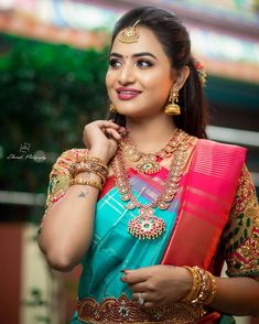 a woman in a blue and pink sari with gold jewelry on her neck, posing for