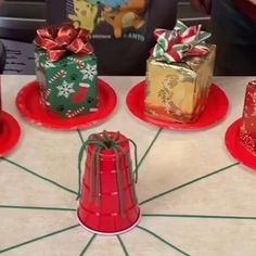 four small christmas gifts on red plates with green and gold wrapping paper around them, sitting on a table