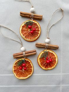 three orange slices with cinnamon sticks and holly on them are hanging from twine strings