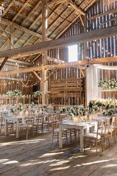 the inside of a barn with tables and chairs set up for a wedding reception in white linens