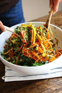 a person is holding a wooden spoon over a bowl of salad with carrots and broccoli