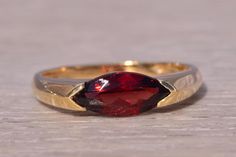 This stunning piece, known as The Crimson Marquise Ring, features a captivating marquise-cut garnet at its center set east to west. The rich, deep red garnet is elegantly set in a 14 karat yellow gold band, designed with sleek, modern lines that add a touch of sophistication. The ring is currently a finger size 7 but can be adjusted to any finger size for an additional charge upon request, ensuring a perfect fit. Love this piece, but don't have the money to spend right now? We offer FREE layaway on every item in our shop. With just 20% down, take one full year (interest-free) to pay off your new jewelry! There are no hidden fees or charges, ever. For more information on our layaway policy, please contact us. Each piece has been hand-selected and meticulously identified and graded by a Grad Garnet Wedding Rings, Garnet Wedding, Cut Orange, Red Rings, Garnet Engagement Ring, Marquise Ring, Garnet Rings, Red Garnet, Deep Red